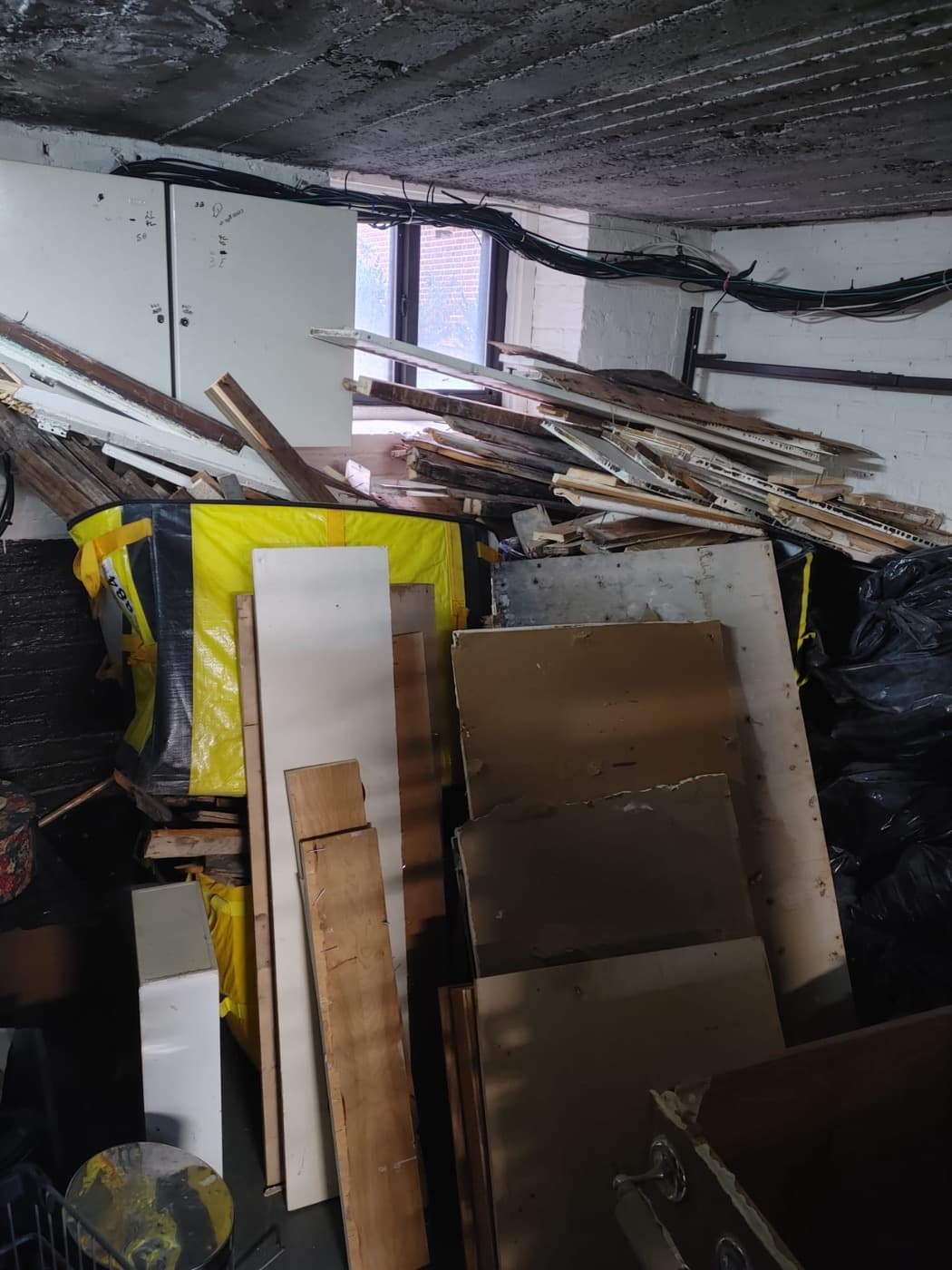 A basement corner filled with scrap lumber, drywall, trim and broken shelving.