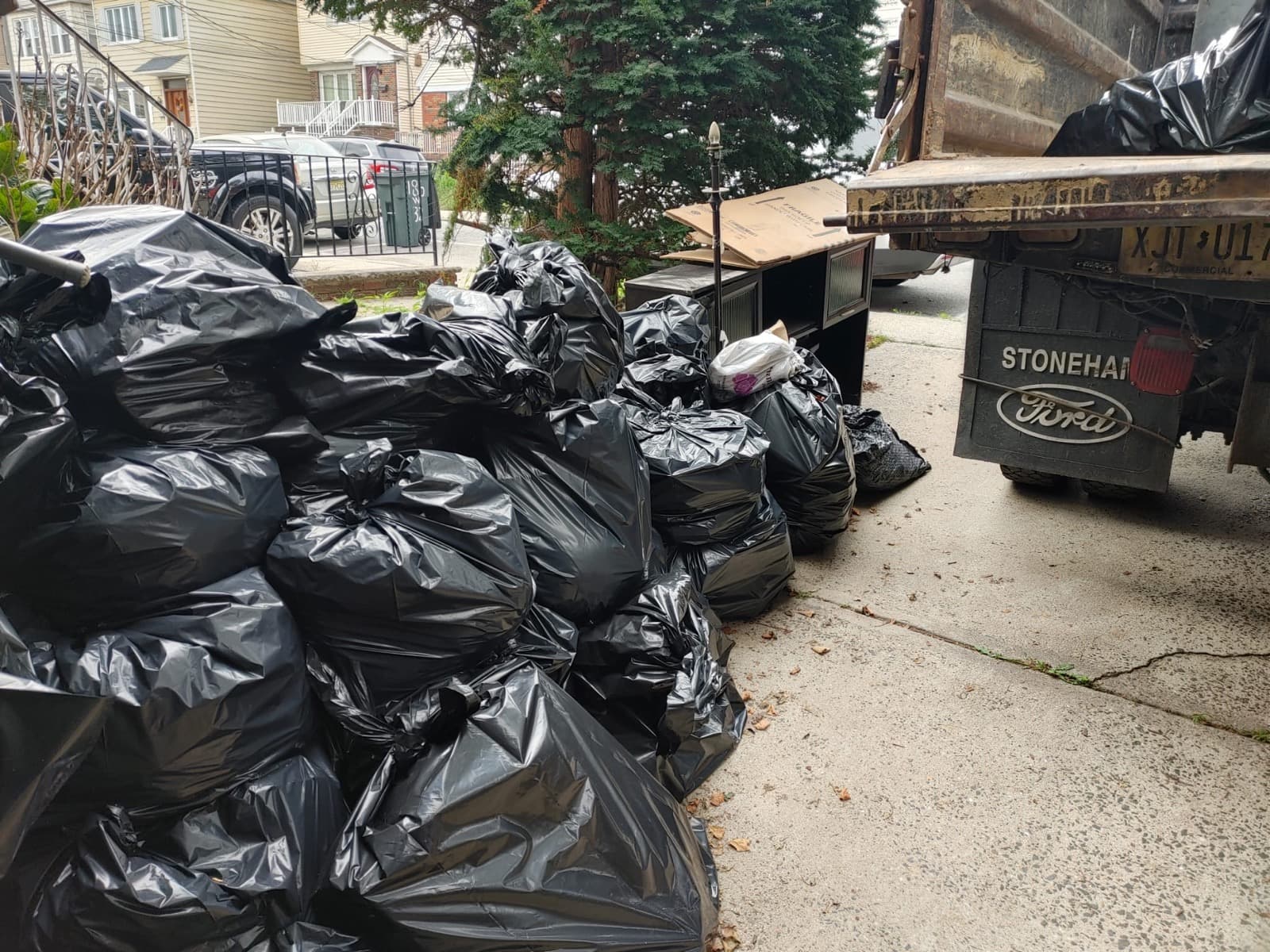 A driveway lined with dozens of filled black contractor bags next to a Ford dump truck.