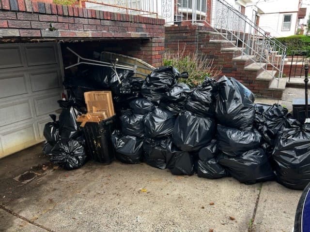 A garage entrance and driveway stacked wall to wall with filled black trash bags.